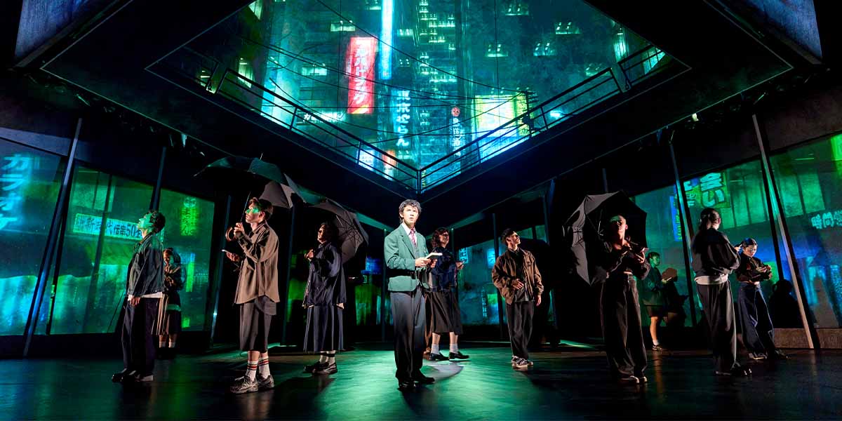 A dramatic scene from "Death Note The Musical" featuring characters in dark costumes against a dimly lit background.