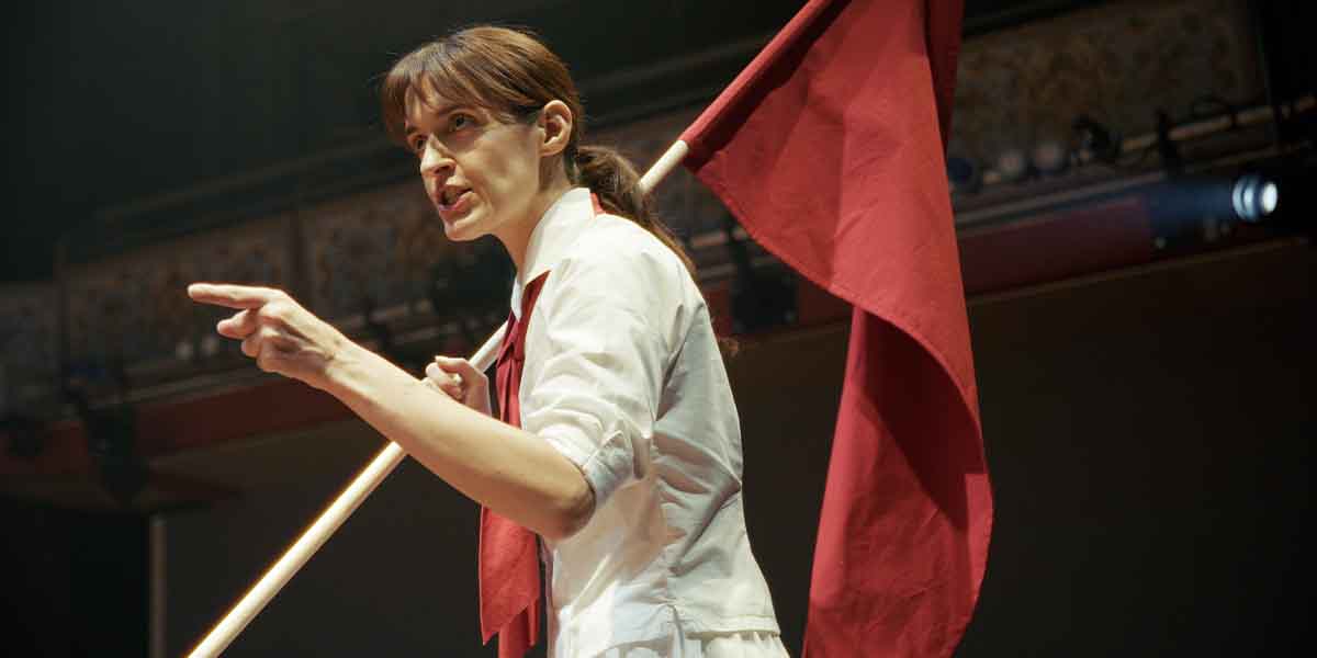 A performer in a white shirt and red tie passionately gestures while holding a red flag.