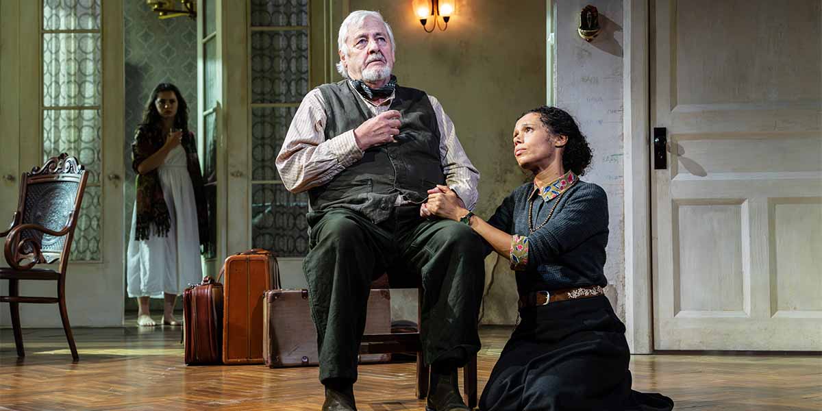 Anastasia Martin stands in the background, while Peter Wight sits, and Vinette Robinson kneels beside him.