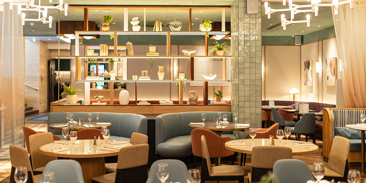A modern kitchen bar featuring wooden counters, stylish stools, and a vibrant atmosphere with patrons enjoying drinks.