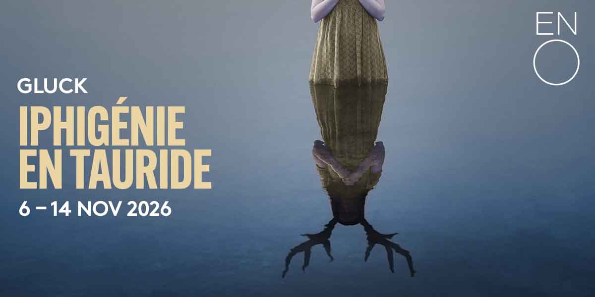 A figure in a long, patterned dress stands in water, reflecting an antlered silhouette beneath.