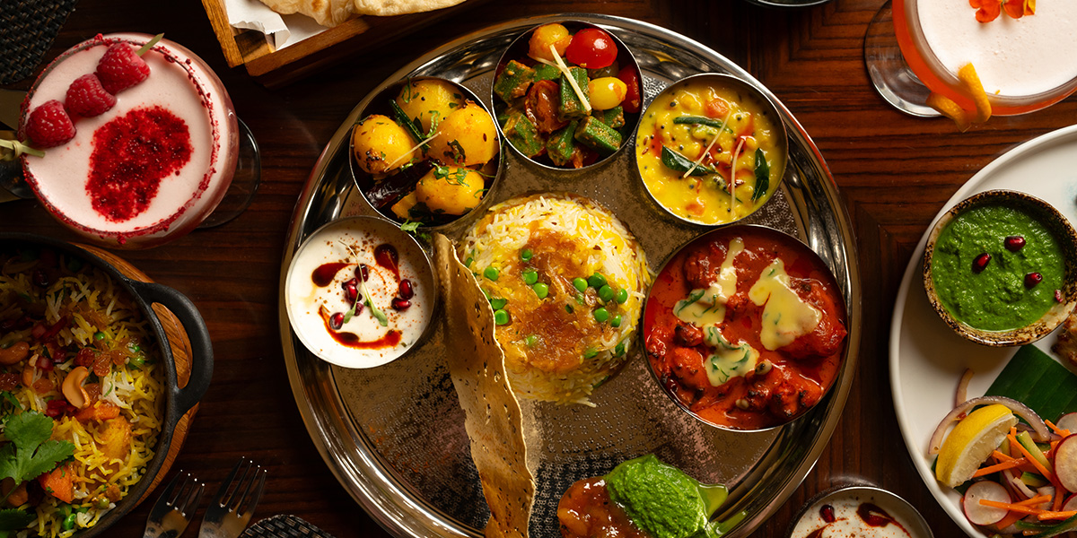 A vibrant thali featuring various Indian dishes, including curries, rice, and naan, on a decorative plate.