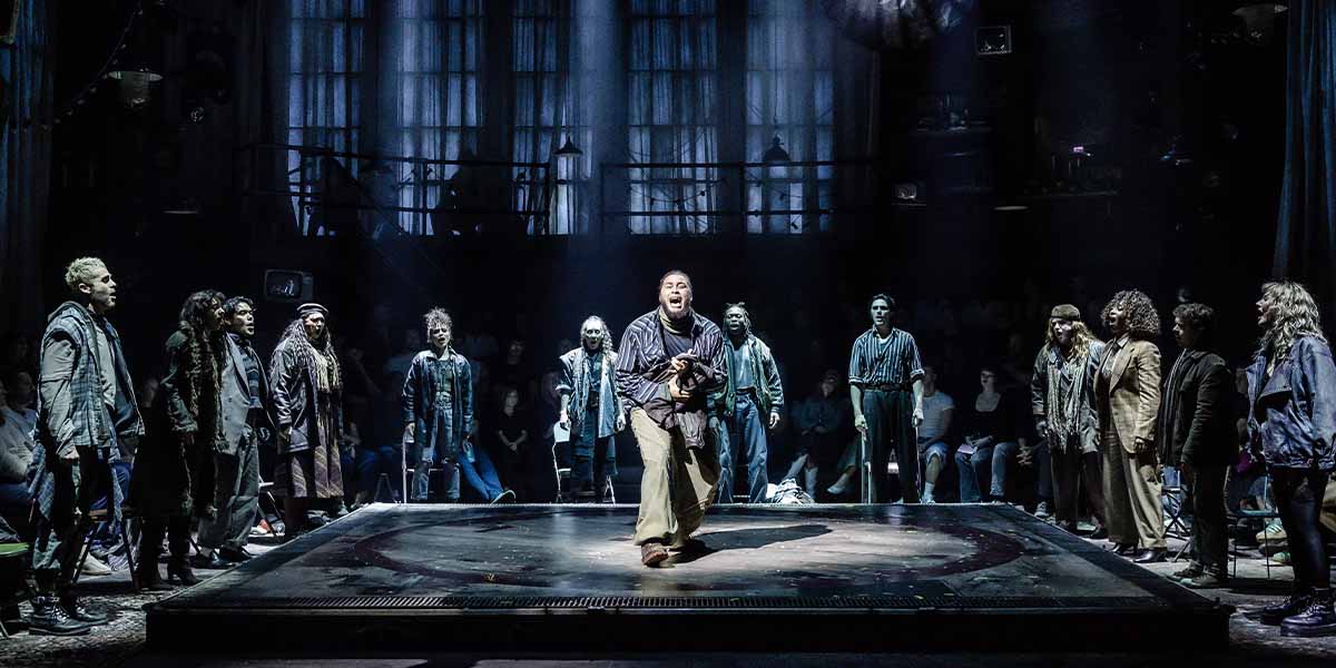 Billy Nevers as Collins performs with the cast of RENT, showcasing vibrant costumes and dynamic poses.