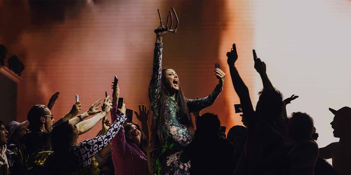 A performer in a sparkling outfit raises claws, surrounded by an enthusiastic crowd at a vibrant event.