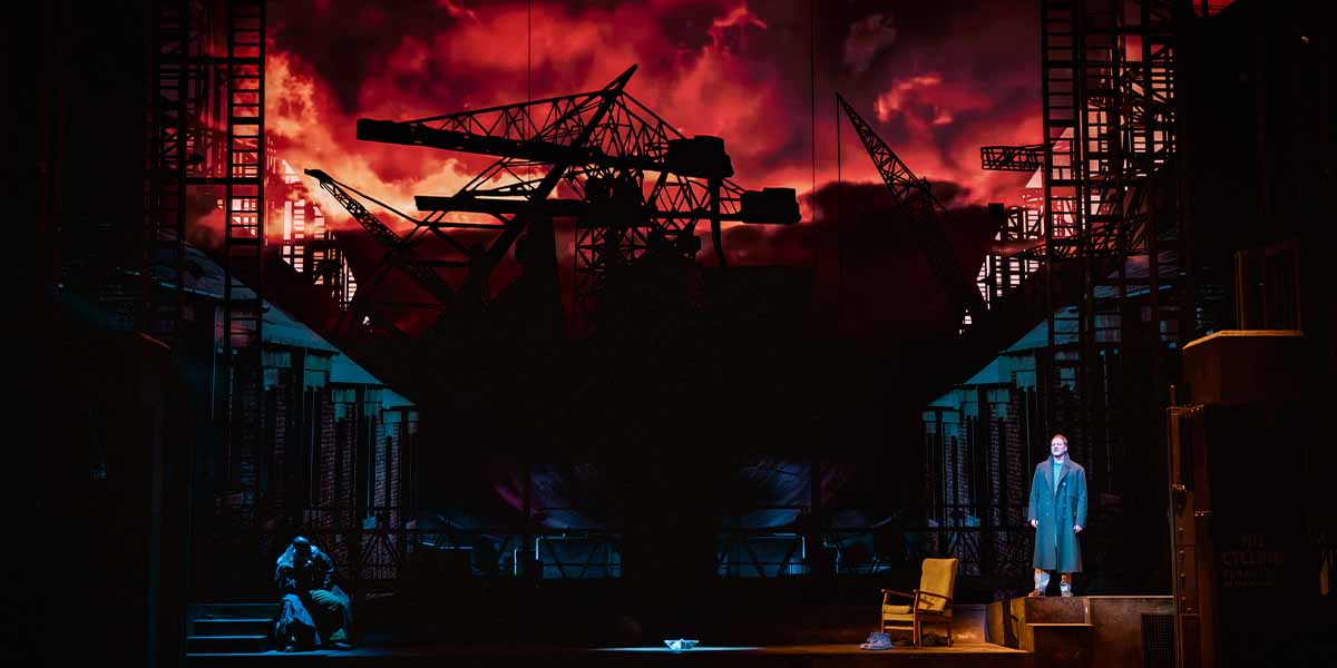 A dramatic stage scene from The Last Ship, featuring a man in a coat against a fiery backdrop.