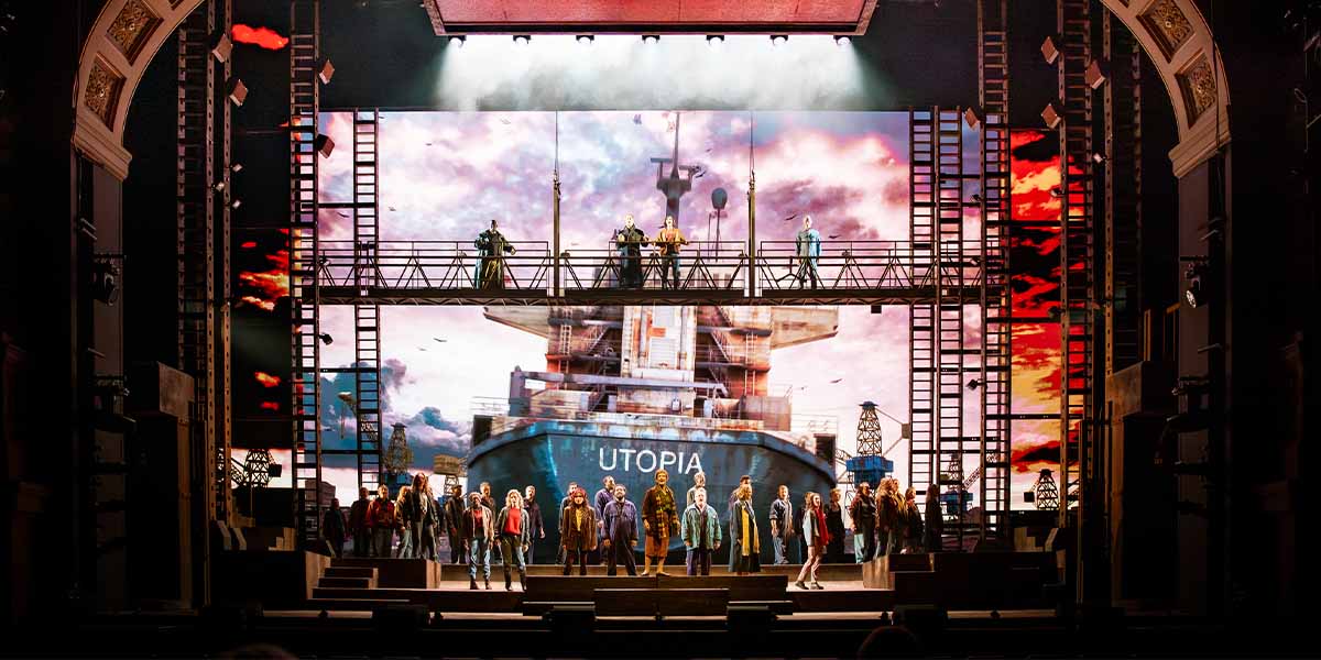 The ensemble cast of The Last Ship poses together, wearing costumes, with a backdrop of stage lights.