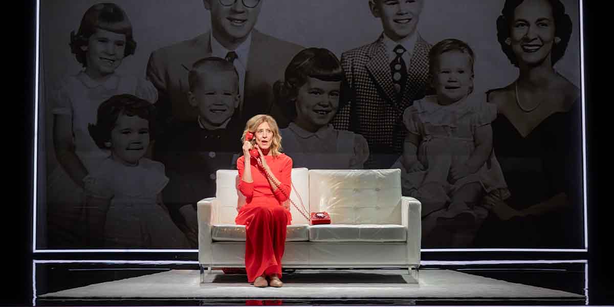 A person in a red dress sits on a white sofa, holding a red telephone, with a black-and-white family photo backdrop.