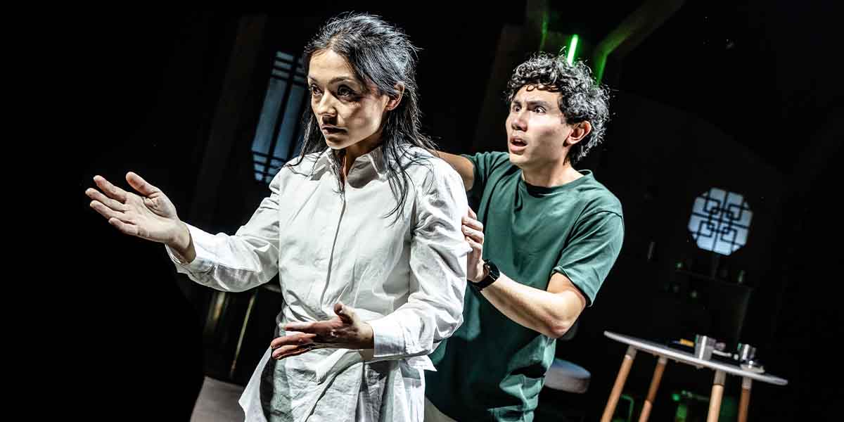 A woman in a white shirt gestures expressively while a man in a green shirt looks concerned.
