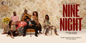 A diverse group of seven people poses together, seated and standing, against a floral wallpaper background.