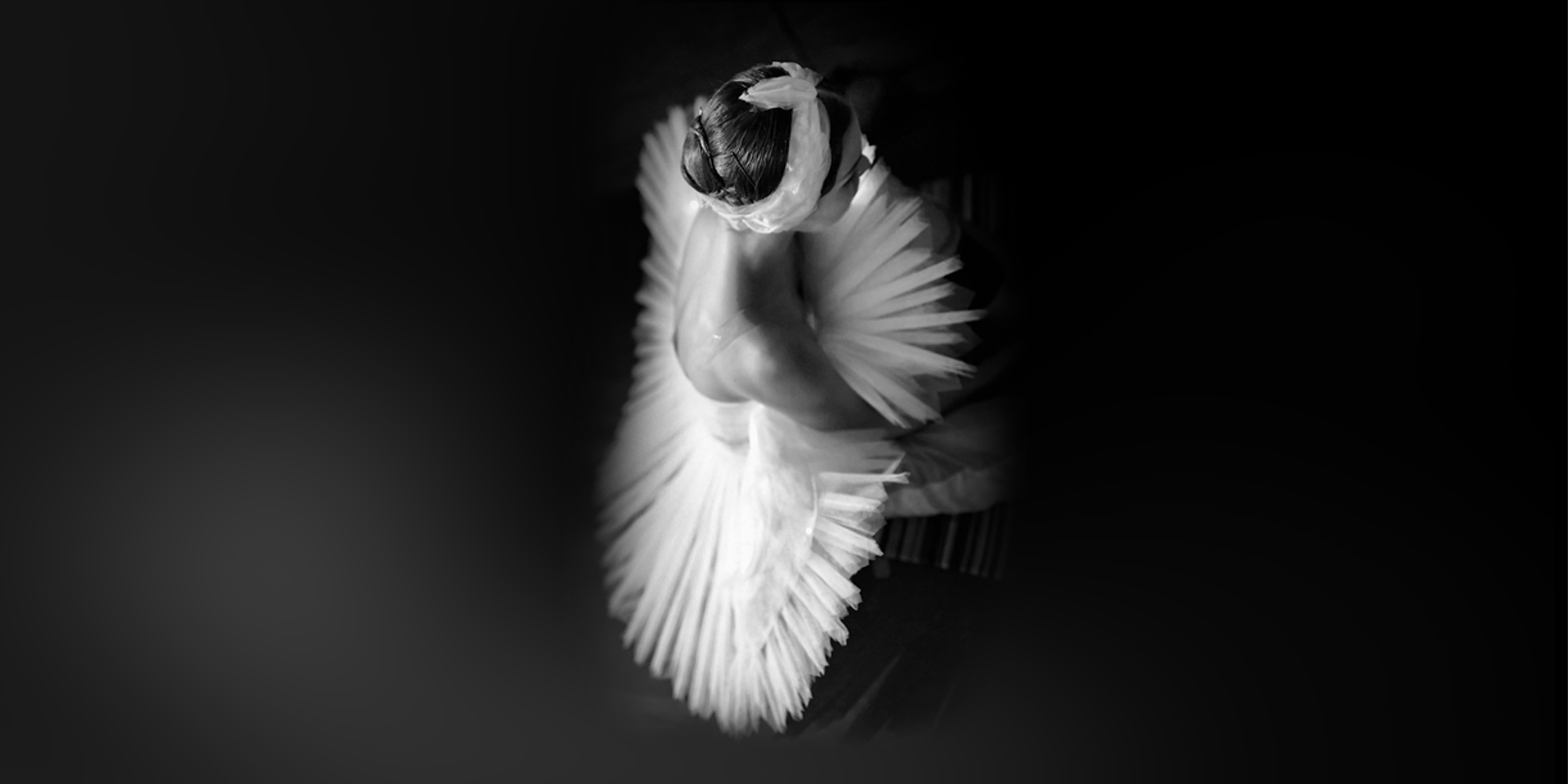 A ballet dancer in a white tutu poses gracefully, viewed from above against a dark background.