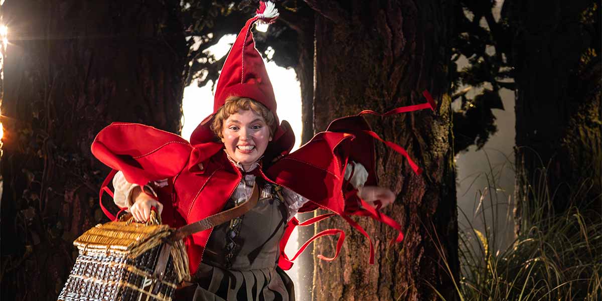 Gracie McGonigal, wearing a red hooded costume, joyfully runs with a basket in a forest setting.