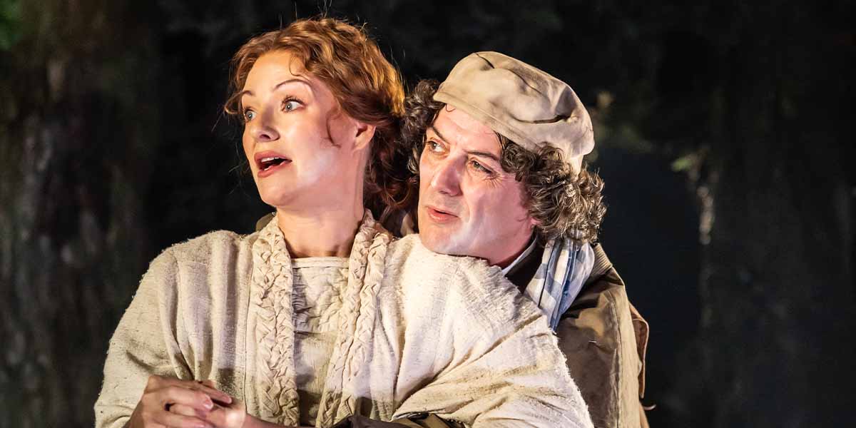 Laura Pitt-Pulford and John Dagleish perform in "Into The Woods," set against a dark forest backdrop.