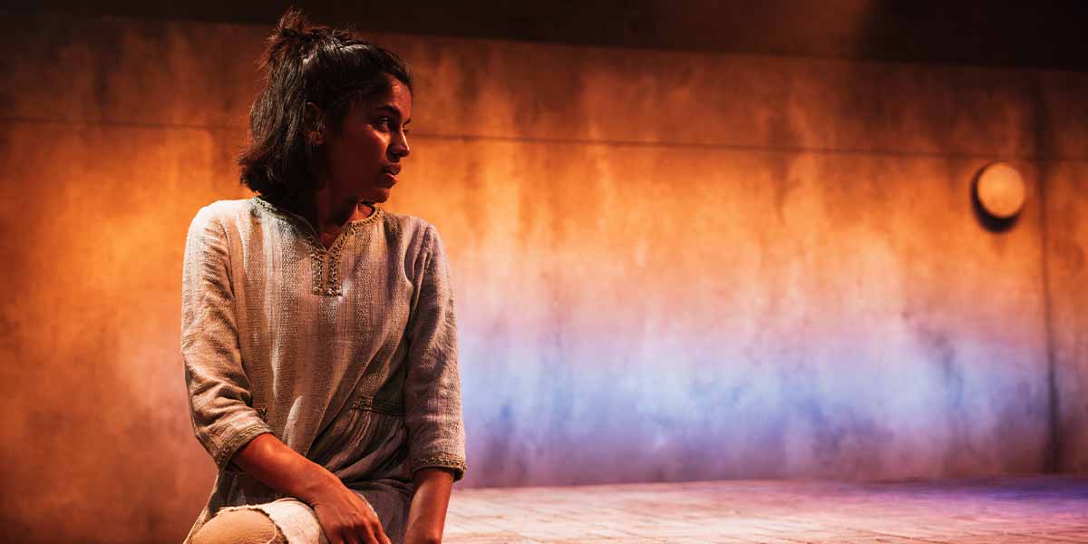 Linnea Berthelsen, seated and contemplative, wears a light-coloured garment against a softly lit, textured backdrop.