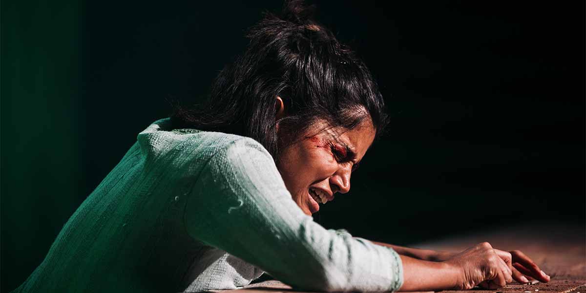 Linnea Berthelsen, portraying 'She', leans over a table, expressing intense emotion with visible distress.