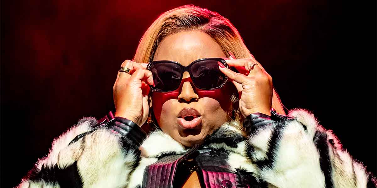 Marisha Wallace, wearing sunglasses and a fur coat, performs passionately against a dramatic red backdrop.