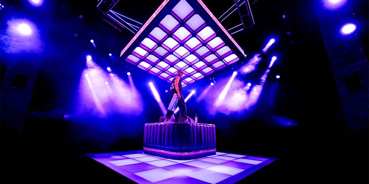 Michael Rishawn performs on a raised platform under vibrant purple lighting in a theatrical setting.