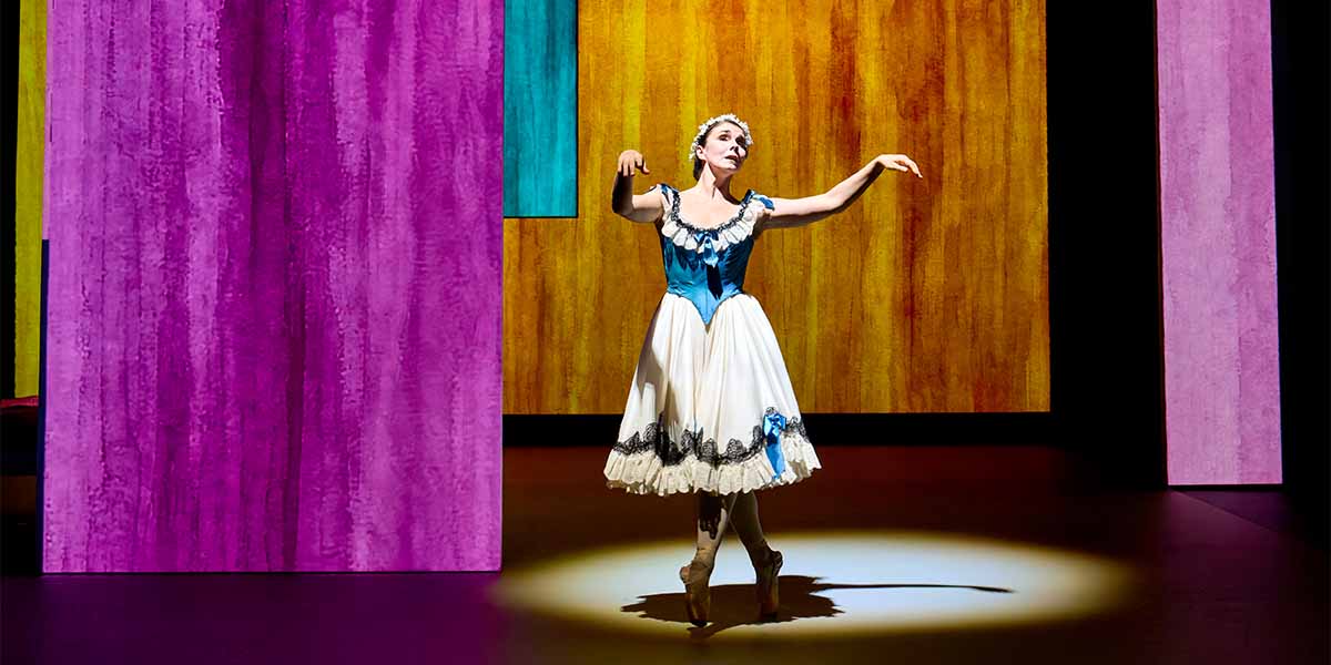 Natalia Osipova performs in a blue and white dress, surrounded by vibrant coloured backdrops.