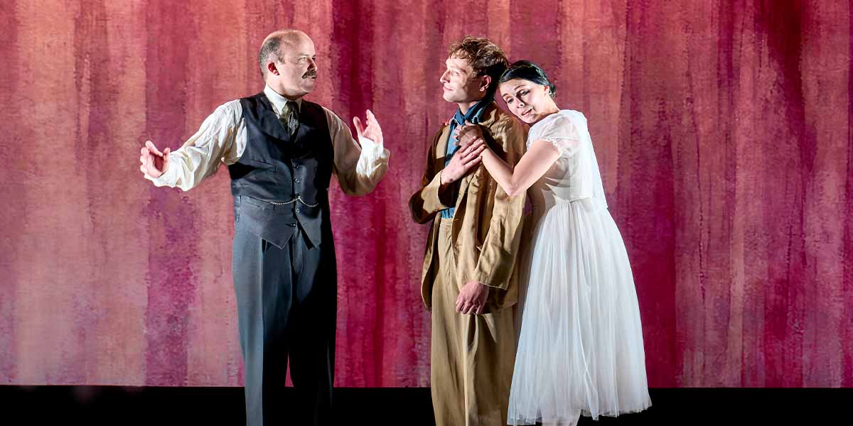 Rory Kinnear gestures expressively while Thomas Flynn and Natalia Osipova interact closely against a pink backdrop.