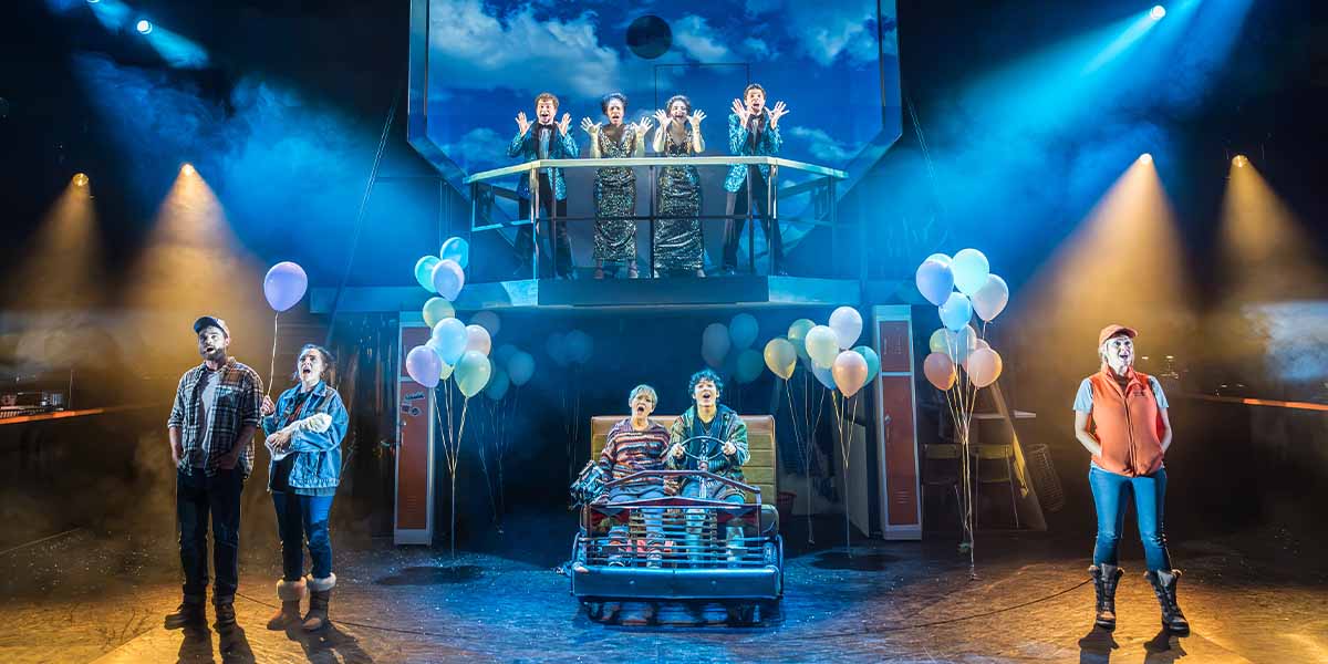 The cast of Kimberly Akimbo poses together on stage at Hampstead Theatre, dressed in colourful costumes.