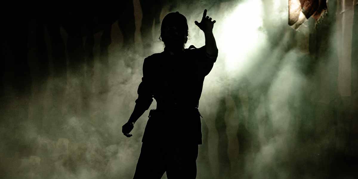 A silhouetted figure gestures dramatically amidst a smoky backdrop, illuminated by soft, diffused lighting.