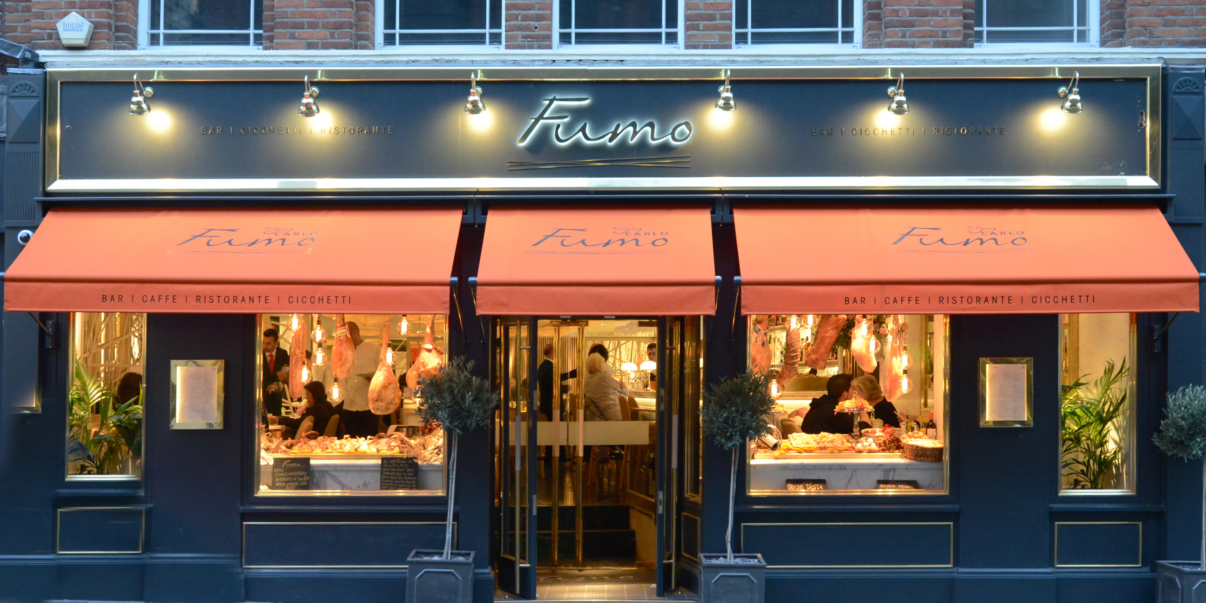 Current image: The exterior of Fumo restaurant features a modern design with large glass windows and a vibrant awning.
