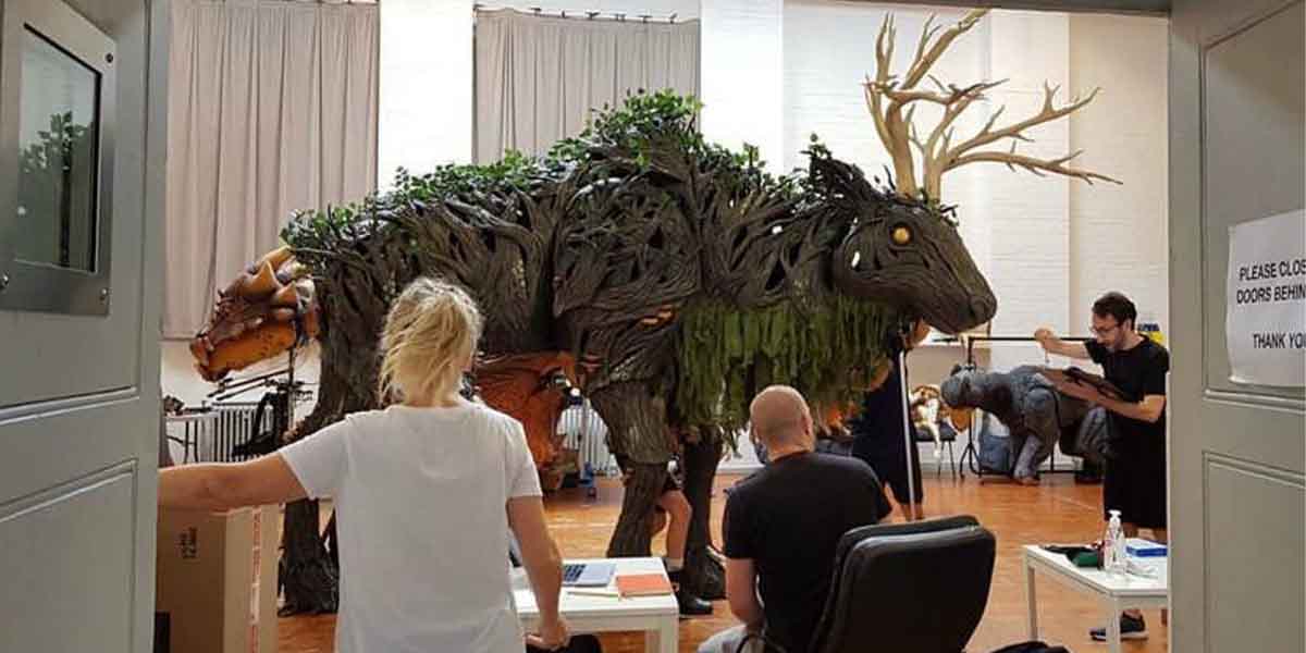 A large, intricate creature sculpture made of branches and foliage is being assembled in a studio.
