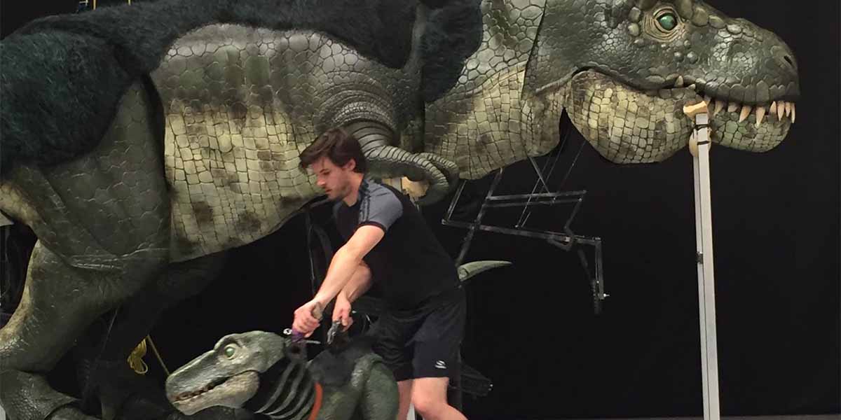 Max Humphries operates a dinosaur puppet, with a large T-Rex model in the background.