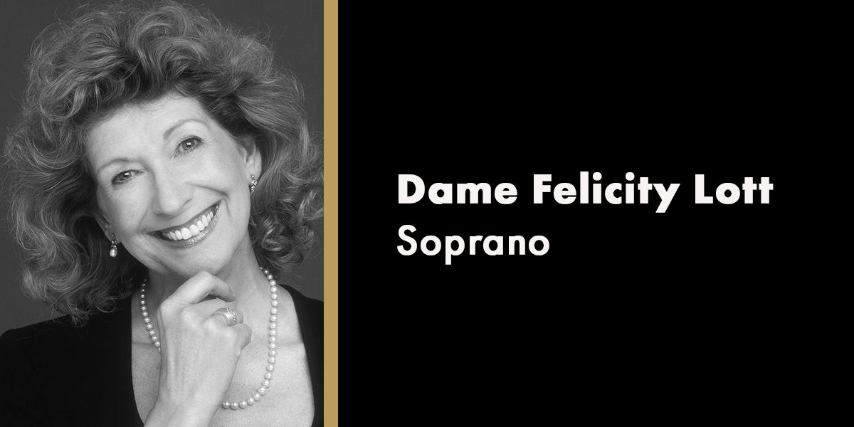 Dame Felicity Lott smiles warmly, wearing a black dress, with a soft-focus background of flowers.