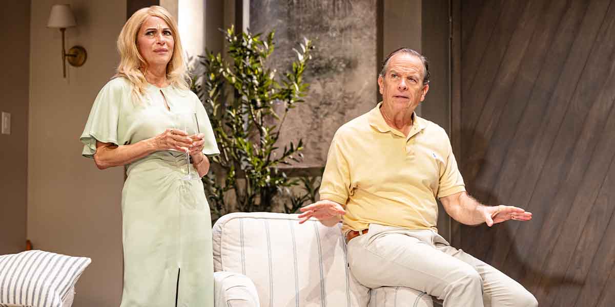 Juliet Cowan, in a light green dress, stands with a drink, while Donald Sage Mackay gestures from a sofa.