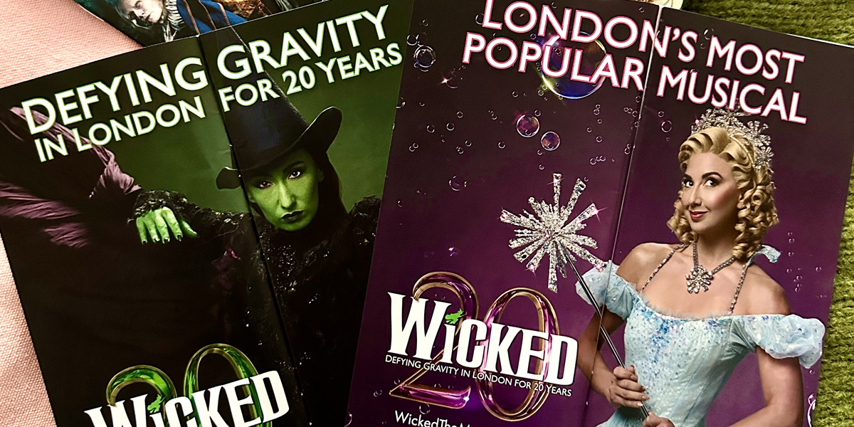 Cast members celebrate the 20th anniversary of Wicked, wearing vibrant costumes, with a festive backdrop.