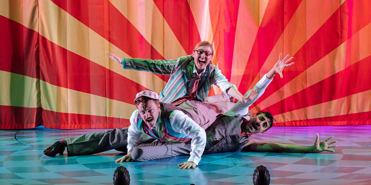 Jonny Weldon, Bronté Barbé, and Richard David-Caine perform energetically on stage against a vibrant backdrop.