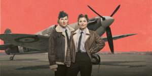 A group of women in vintage attire poses confidently with a Spitfire aircraft in the background.